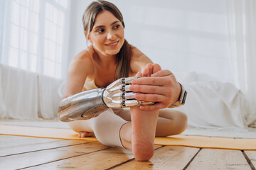 Smiling young woman with contemporary bionic prosthesis arm does yoga exercises on yellow mat near...