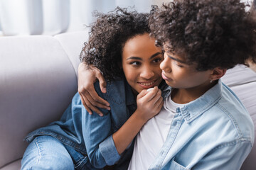 Smiling african american woman hugging curly boyfriend on couch