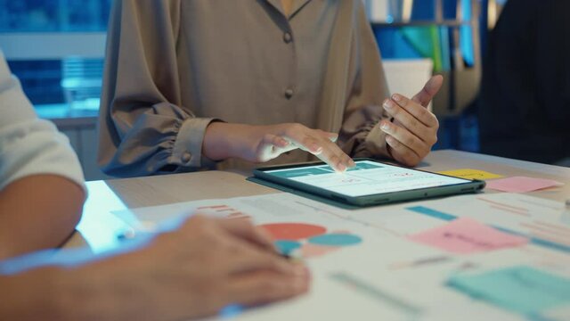 Group of Asia young creative people in smart casual wear discussing business brainstorming meeting ideas mobile application software design project in modern night office. Coworker teamwork concept.