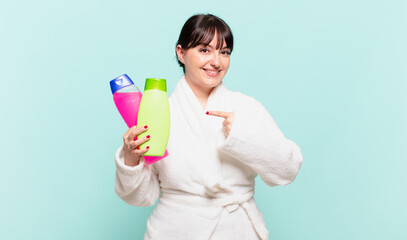 young woman wearing bathrobe smiling cheerfully, feeling happy and pointing to the side and upwards, showing object in copy space