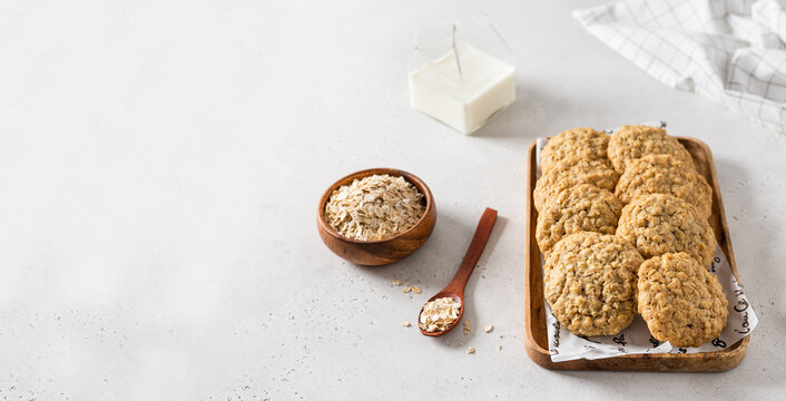 Homemade oatmeal cookies with banana, oats and nuts on a wooden tray and oats flakes on white background, side view, copy space. Healthy food. Oatmeat biscuits recipe