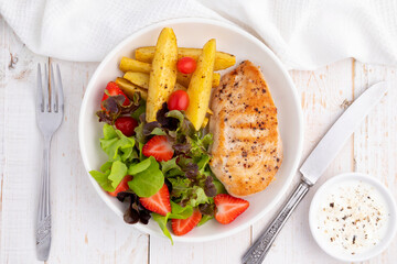 Healthy grilled chicken breast served with grilled potatoes, strawberries and fresh vegetables like lettuce, green oak, red oak and tomatoes. This is good for clean eating. 