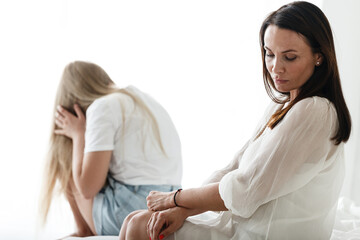 Obraz premium Family conflict and relations concept. Mother and daughter having quarrel and aguring at home. Sad woman and teenage girl sitting on bed. Not looking at each other