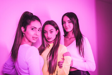 Lifestyle of friends partying in a nightclub with pink neon lights, portrait of young beautiful Caucasian women looking at camera