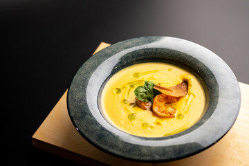 Cream pumpkin soup with grilled shrimp. Soup in a blue plate on a black background.