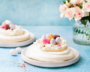 Meringue nest cake with colorful chocolate eggs, buttercream frosting on light blue background with copy space. Selective focus. Food ideas for kids. Easter cake. Spring love feast concept. Close up.