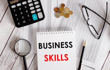BUSINESS SKILLS written in a white notepad near a calculator, cash, glasses, a magnifying glass and...