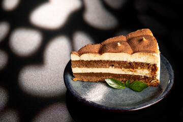Italian sweet dessert tiramisu on a plate on a black background with mint leaf.