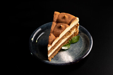 Italian sweet dessert tiramisu on a plate on a black background with mint leaf.