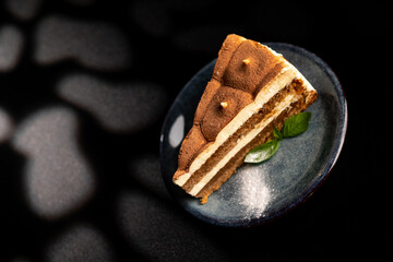 Italian sweet dessert tiramisu on a plate on a black background with mint leaf.