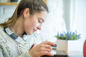 Young beautiful long-haired girl uses a mobile device in a cafe.