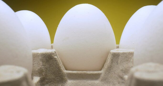 extreme close-up of white eggs in carton on yellow background.