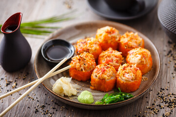 Baked sushi maki rolls with salmon, crab, cucumber, avocado, flying fish roe and spicy sauce on a plate with chopsticks, soy sauce, wasabi and ginger. Japanese seafood served for lunch in restaurant