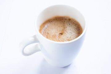 Cup of coffee with handle, isolated on a white table. Seen obliquely from above. Focus on the froth of the coffee. CUP WITHOUT SAUCER