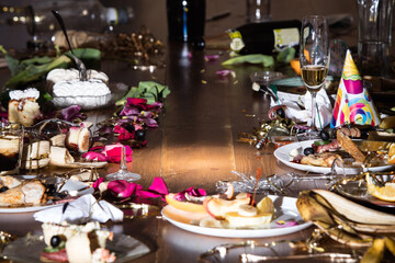 Early morning after the party. Glasses and plates on the table with confetti and serpentine, leftovers, flower petals