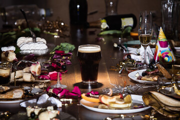 Early morning after the party. Glass of dark, cold stout, beer on the table with confetti and serpentine, leftovers, flower petals