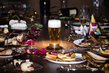 Early morning after the party. Glass of light, cold lager, beer on the table with confetti and serpentine, leftovers, flower petals