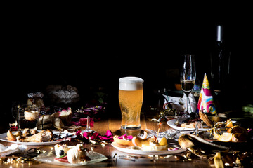 Early morning after the party. Glass of light, cold lager, beer on the table with confetti and serpentine, leftovers, flower petals