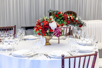 Fancy table set for dinner with flower composition in restaurant, luxury interior background. Wedding elegant banquet decoration and items for food arranged by catering service on white table.