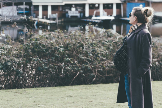 side view of very pregnant blone woman taking a walk by river or lake