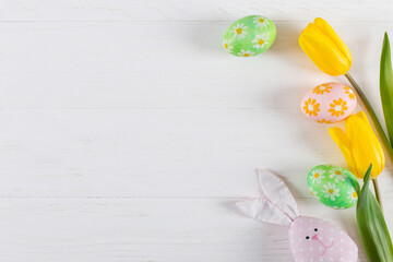 Easter colored eggs, toy rabbit and tulips on a white table. Copy space.