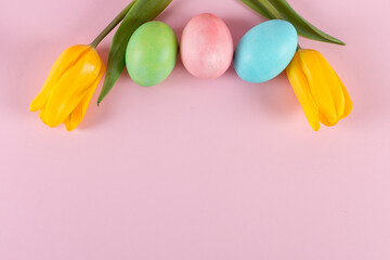 Obraz na płótnie Canvas Easter colored eggs and tulips on a pink background. Copy space.