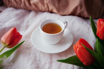 still life with a white cup and tulips on a light fabric