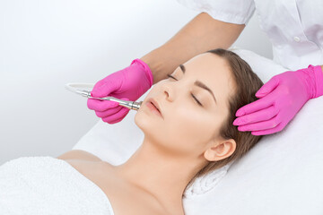 Obraz na płótnie Canvas Cosmetologist makes procedure microdermabrasion on the face against acne and blackheads near the eyes. Women's cosmetology in the beauty salon.