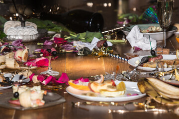 Early morning after the party. Glasses and plates on the table with confetti and serpentine, leftovers, flower petals