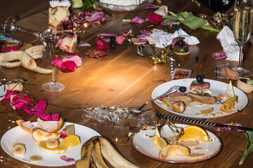 Early morning after the party. Glasses and plates on the table with confetti and serpentine, leftovers, flower petals