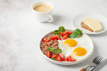 Eggs, buckwheat, tomatoes and spinach on a plate, coffee in cup. Healthy breakfast.