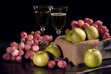 Bunches of pink grapes and green apples on a dark background. A glass of champagne is in the background. Still life. Vitamin basket.