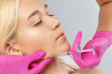 Cosmetologist makes rejuvenating anti wrinkle injections on the face of a beautiful woman. Female...