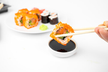 take a california maki rolls with bamboo chopsticks and put in into  soy sauce. pink ginger, wasabi. asian food, japanese cuisine background