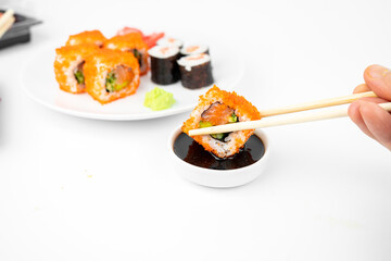 take a california maki rolls with bamboo chopsticks and put in into  soy sauce. pink ginger, wasabi. asian food, japanese cuisine background