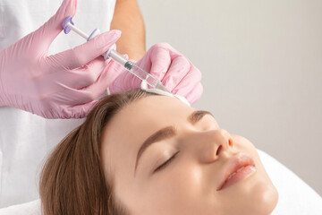 Cosmetologist makes rejuvenating anti wrinkle injections on the face of a beautiful woman. Female...