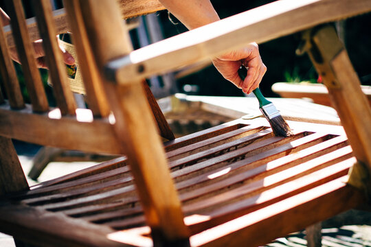 Female hand holding a brush applying varnish paint on a wooden garden chair- painting and caring for wood