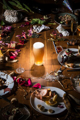 Early morning after the party. Glass of light, cold lager, beer on the table with confetti and serpentine, leftovers, flower petals