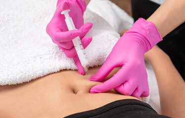 A doctor of aesthetic cosmetology makes lipolytic injections to burn body fat on a woman’s...