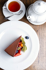 Chocolate dessert with strawberries, blueberries, physalis. White dishes,сup of Black tea. Tea drinking with dessert. flat lay. vertical photo. Piece of cake stuffed with red velvet and cocoa glaze