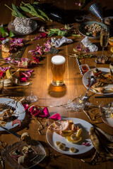 Early morning after the party. Glass of light, cold lager, beer on the table with confetti and serpentine, leftovers, flower petals