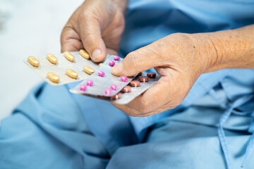Asian senior or elderly old lady woman patient holding antibiotics capsule pills in blister packaging for treatment infection patient in hospital; Pharmacy drugstore concept.