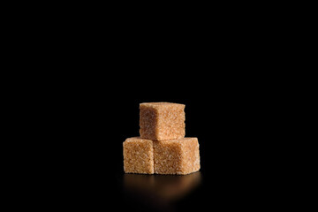 Three cubes of cane sugar on a black background.