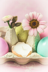 Box with pastel-colored easter eggs, candles in eggshell and spring flower blossoms as Easter decoration, close-up, vertical