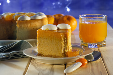 Tangerine cheesecake with meringue discs on white square plate, three tangerines, glass of juice, dessert plate with a piece of cheesecake and a spoon on a wooden table