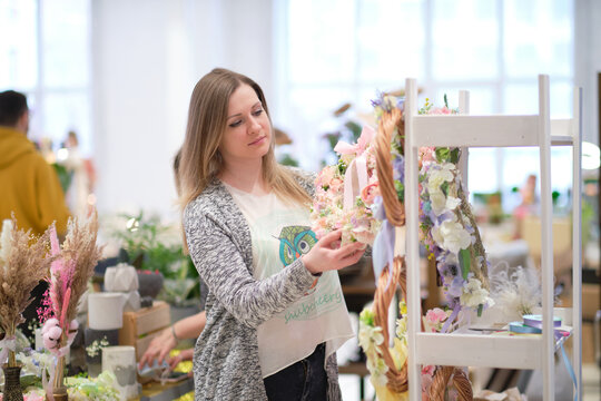 business owner selling behind counter with her bouquet of dried flowers at local market of craftsmen, small business. young woman entrepreneur sells floral holiday composition.
