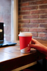 Woman hand holds paper cup of coffee or tea on cafe background. Vertical picture, copy space
