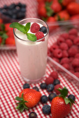 Yoghurt decorated with mint, raspberries and blueberry, on a red and white checkered cloth. With container of raspberries in the background