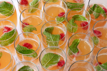 Tall glasses with alcoholic  drink decorated with raspberries and mint