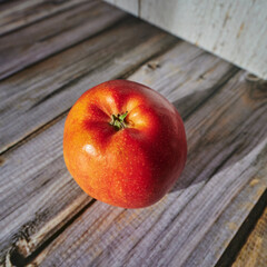 An apple that is lit by the sun and decoratively lies on a wooden surface.